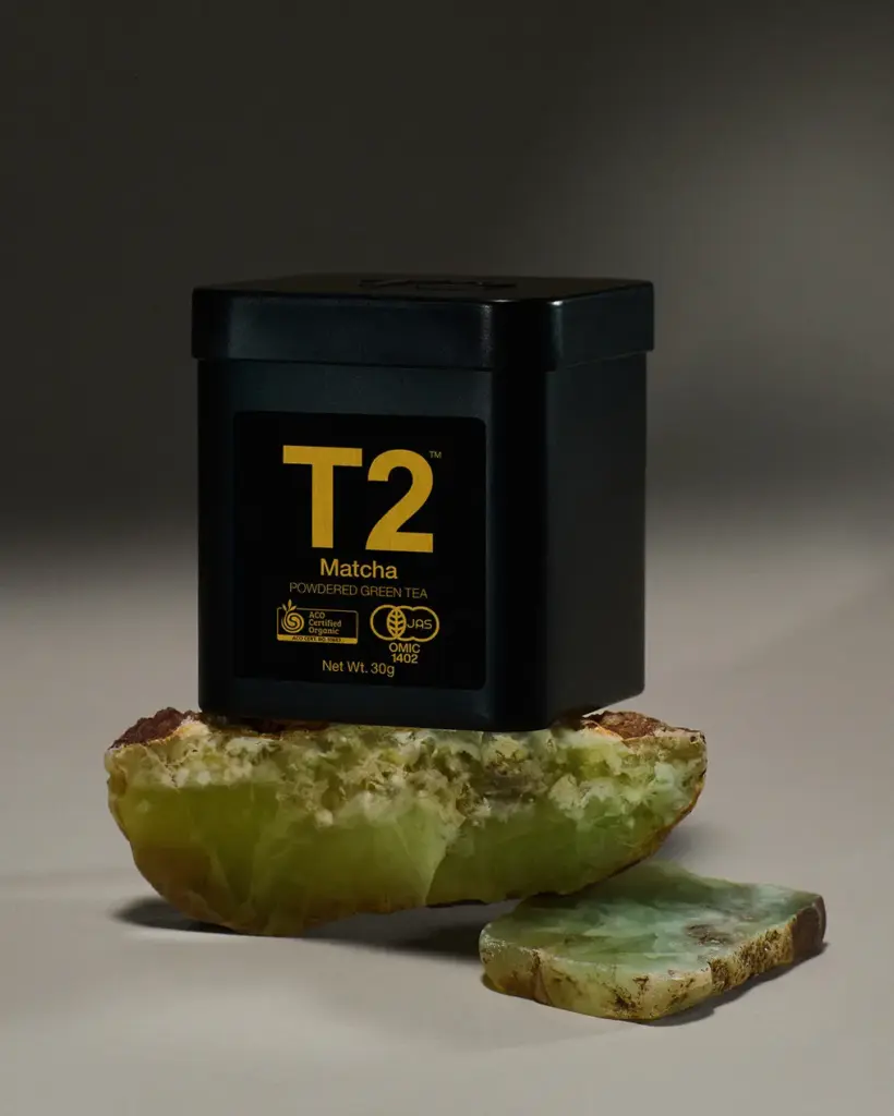 Black T2 Matcha tin with gold lettering displayed on green stone pieces