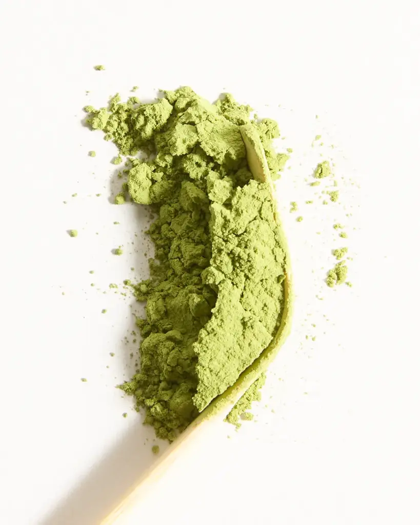 Pale green matcha powder piled on a bamboo scoop against a white background