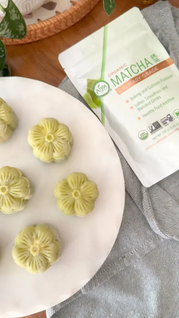 Pale green flower-shaped pastries beside a pouch of Aiya culinary matcha