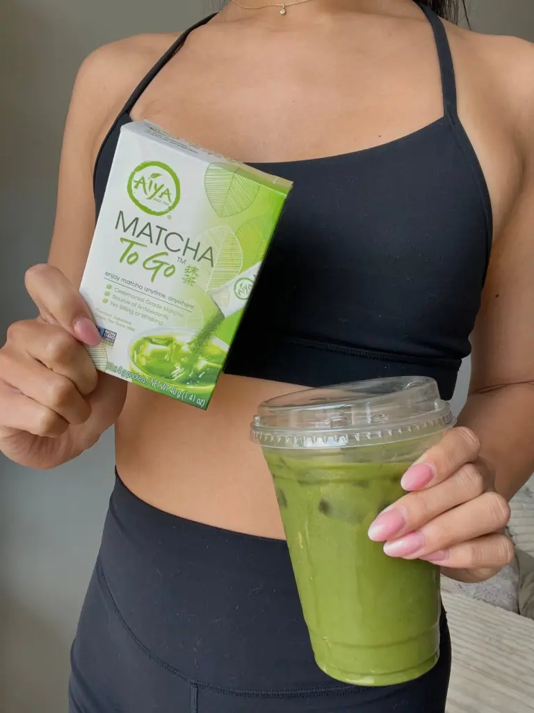 Person holding a Matcha To Go box and a clear cup of iced green matcha