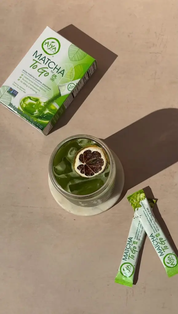 Iced green matcha drink with citrus garnish beside Matcha To Go packets and box