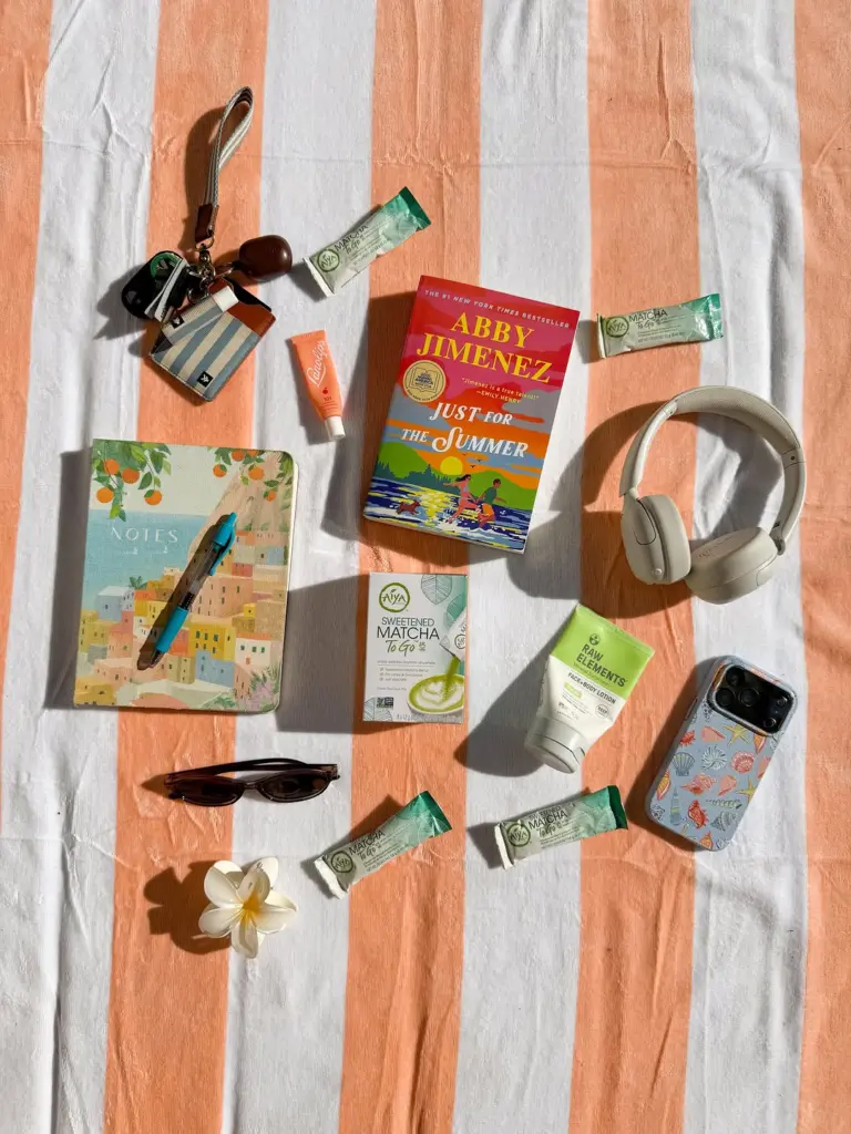 Aiya matcha box and packets arranged with a book, headphones, notebook, sunglasses, and phone