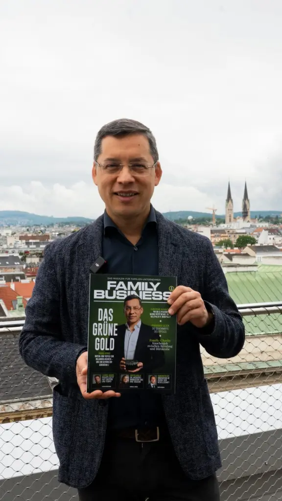 Man wearing glasses holds a Family Business magazine on a rooftop terrace