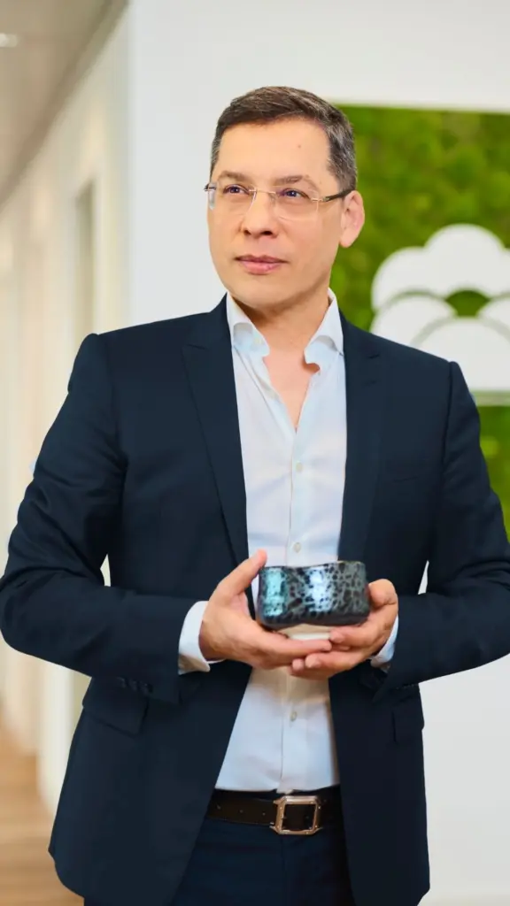 Man in a dark suit and glasses holding a blue ceramic bowl
