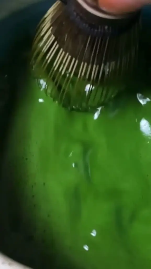 Bamboo whisk stirring bright green matcha in a bowl