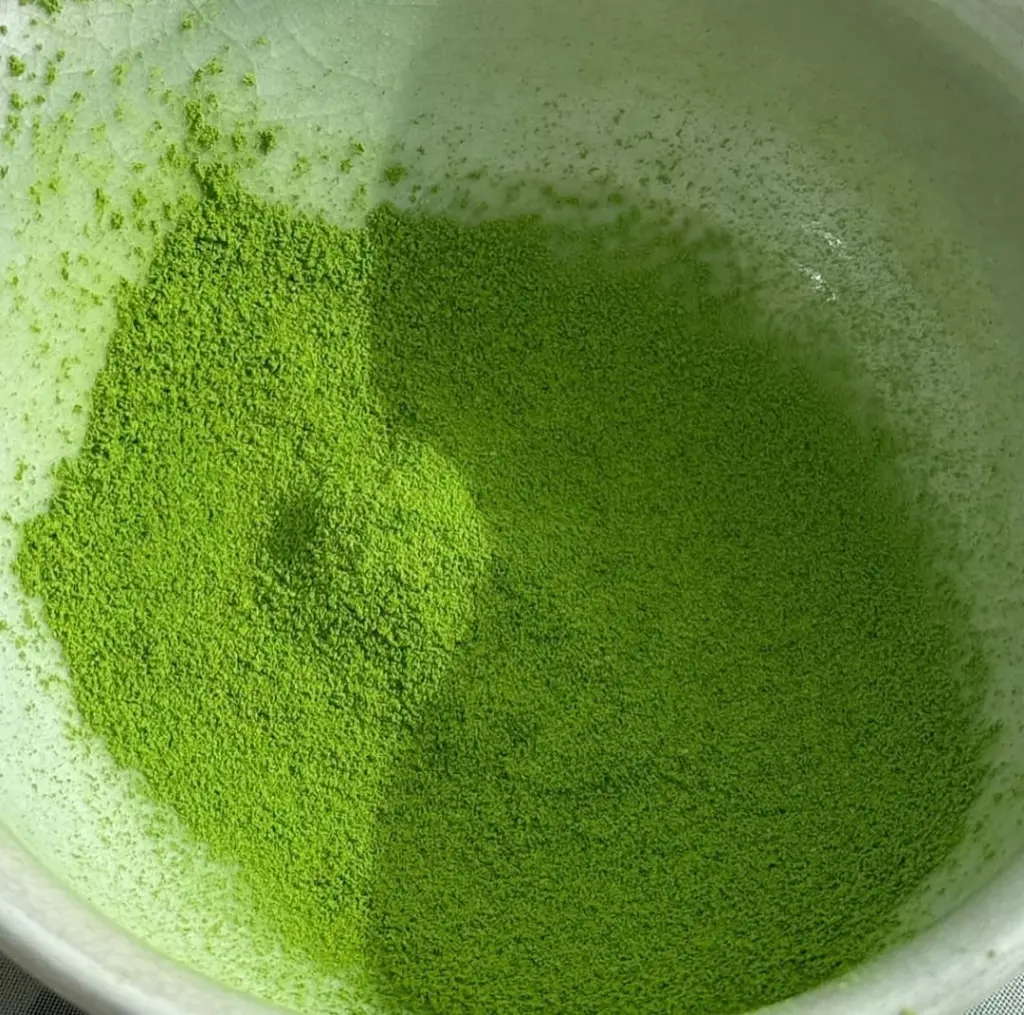 Fine bright green matcha powder spread across a pale bowl