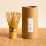 Anatae bamboo matcha chasen beside labeled cylindrical container on bamboo mat