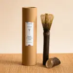 Long-handle bamboo matcha whisk beside Anatae cylindrical packaging and matching stand