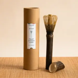 Long-handle bamboo matcha whisk beside Anatae cylindrical packaging and matching stand