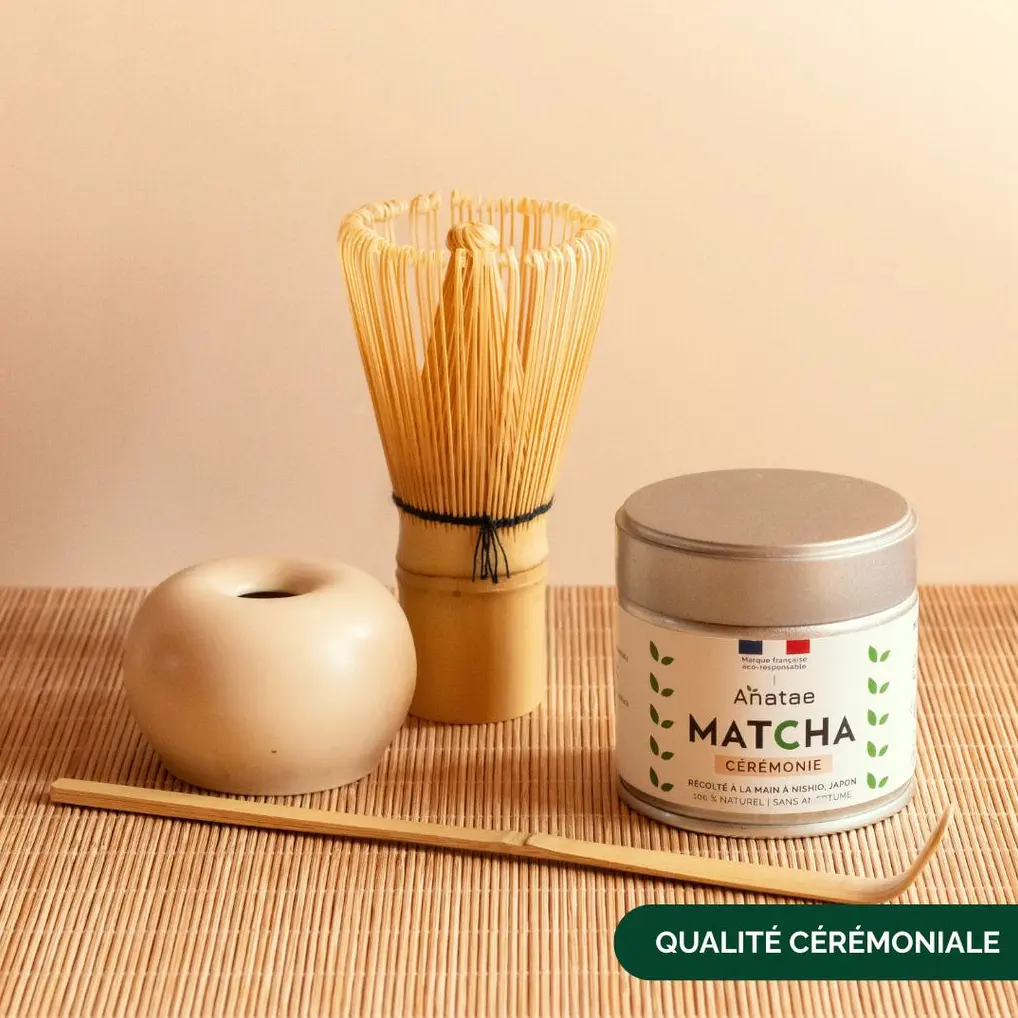 Anatae matcha tin beside bamboo whisk, whisk holder, and scoop on woven mat