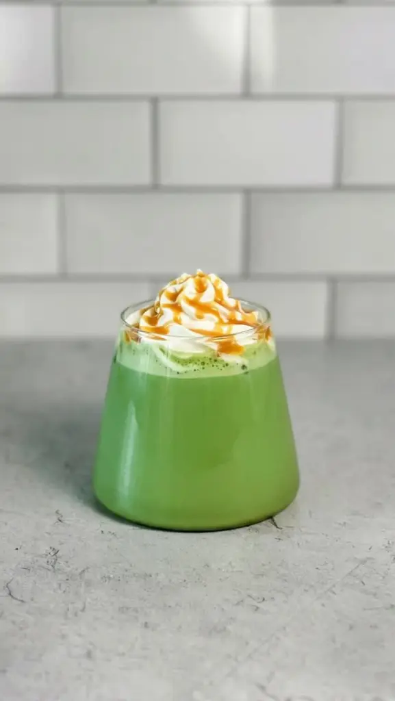 Bright green drink topped with whipped cream and golden drizzle