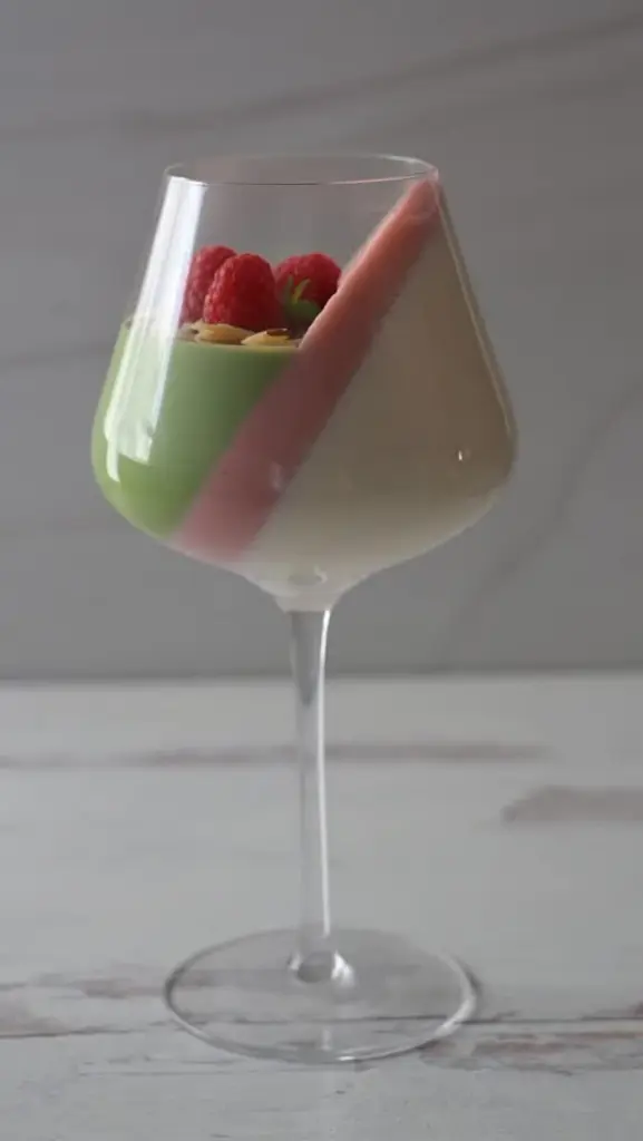 Layered green and white dessert topped with raspberries in a stemmed glass