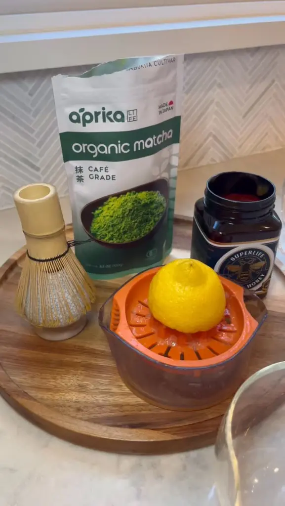 Matcha package, bamboo whisk, lemon on a juicer, and open honey jar