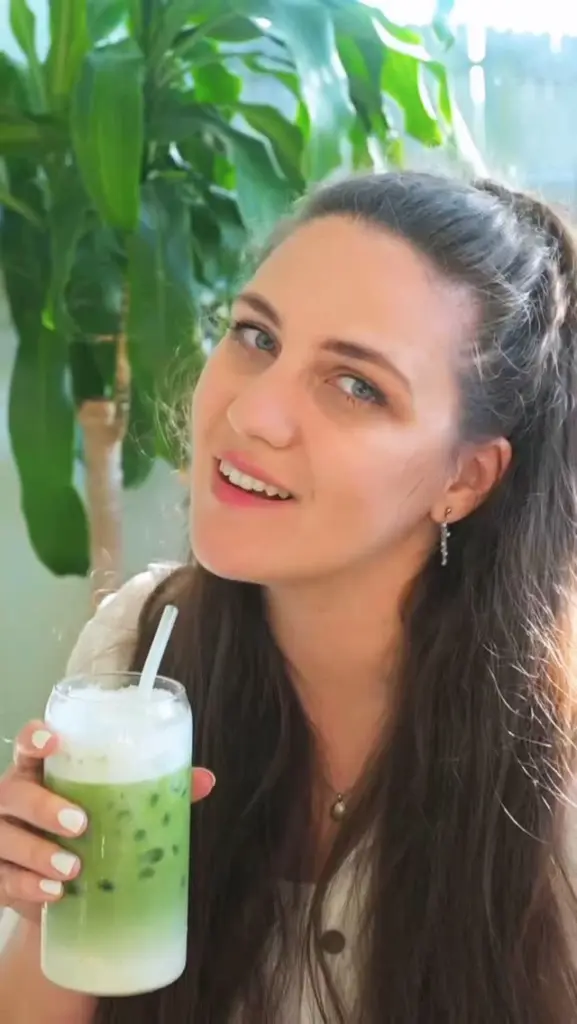 Smiling woman holding a layered iced green drink with foam and a straw