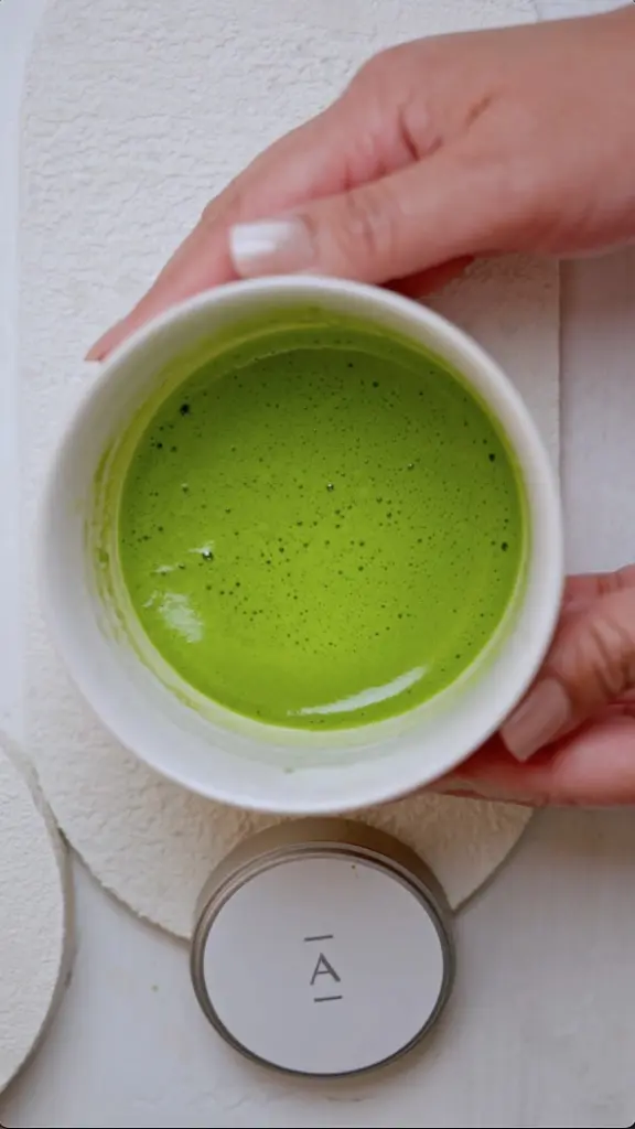 Hands holding a white bowl filled with frothy bright green matcha