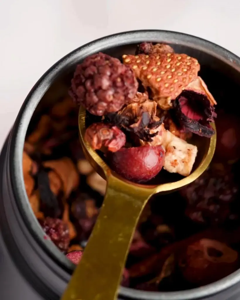 Gold spoon filled with colorful dried fruit pieces above an open tin