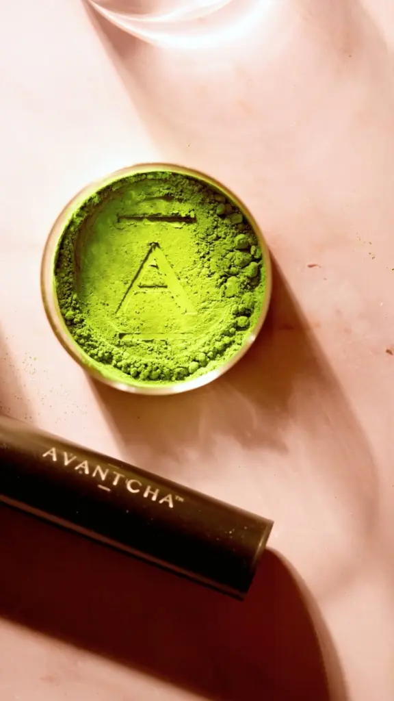 Bright green matcha powder in a round tin with an A mark pressed into the surface