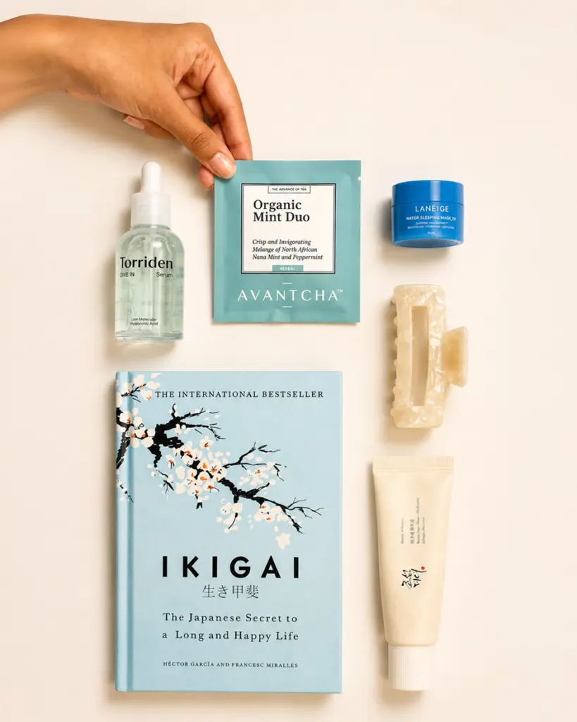 Hand holding an AVANTCHA Organic Mint Duo packet among a book, skincare items, and a hair clip