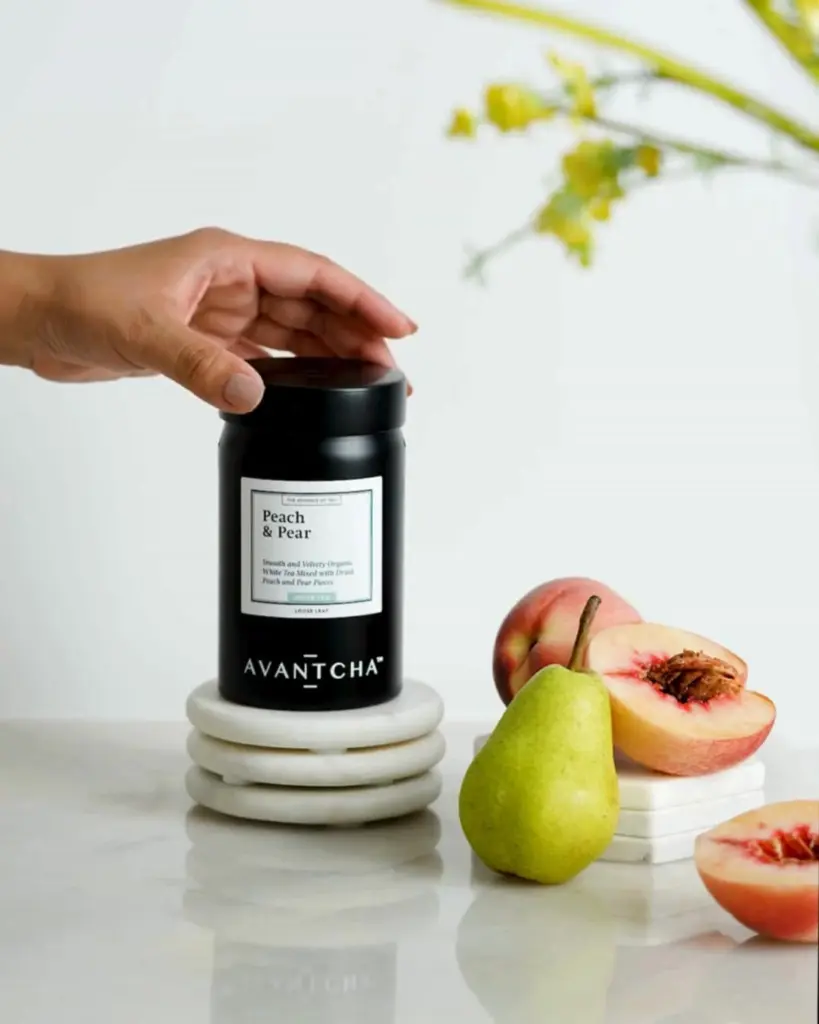 Black AVANTCHA Peach & Pear tea canister beside peaches and a green pear