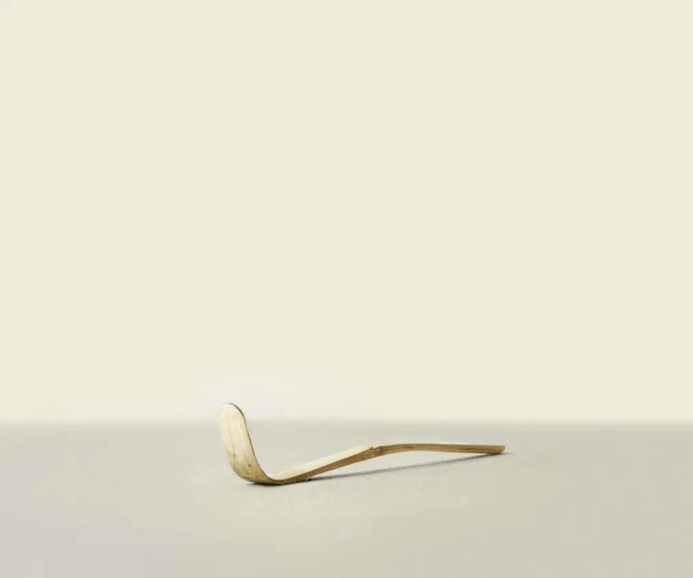 Curved bamboo matcha scoop resting on a light surface