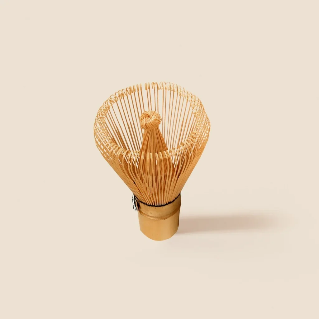 Pale bamboo matcha whisk standing upright, fanned tines curling outward around a knotted center core