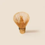 Pale bamboo matcha whisk standing upright, fanned tines curling outward around a knotted center core
