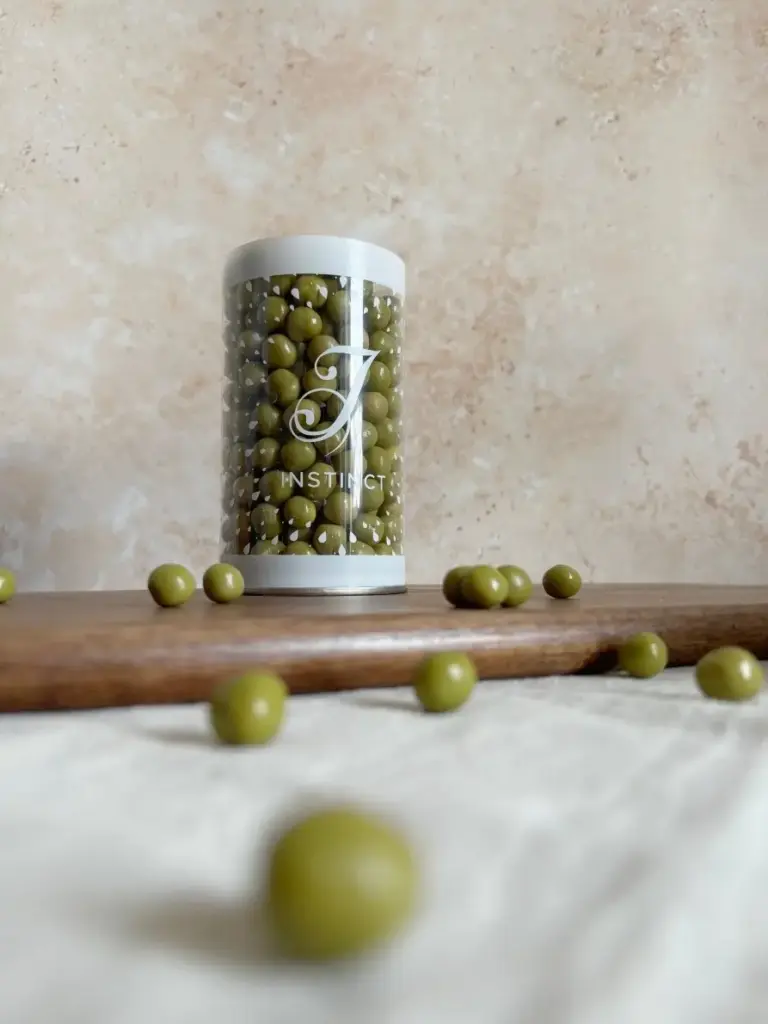 Clear Instinct container filled with green confectionery balls, with several pieces scattered on a wooden board
