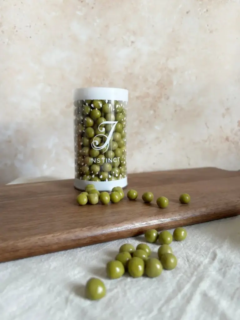 Clear Instinct container filled with green-coated spheres, with more pieces scattered on a wooden board