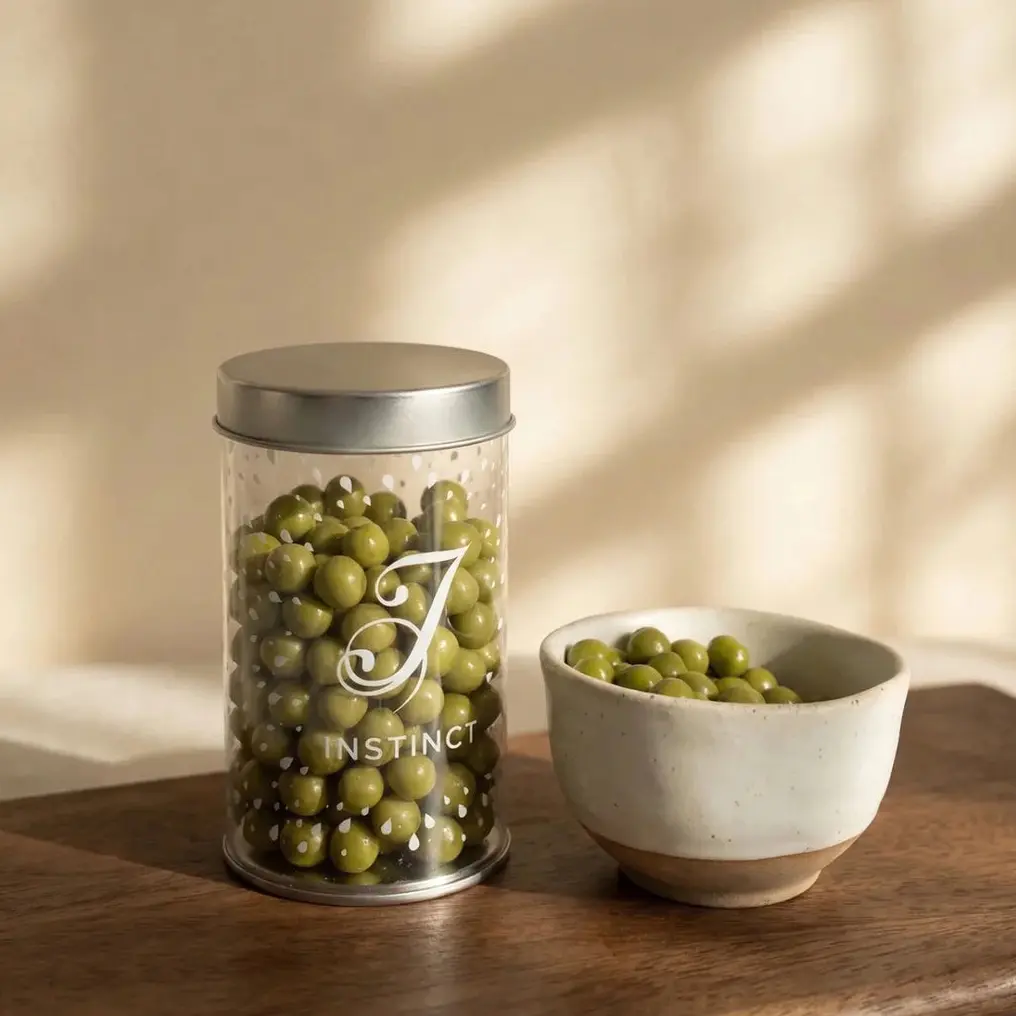 Green matcha-coated chocolate balls in a clear Instinct jar beside a ceramic bowl