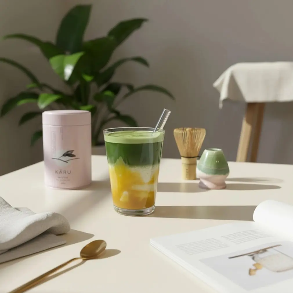 Bio Matcha Mittsu tin beside a layered green and yellow iced drink, bamboo whisk, and ceramic whisk holder