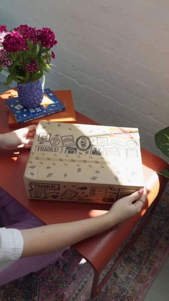 Hands holding a decorated Bird & Blend Tea Co. cardboard box on an orange table