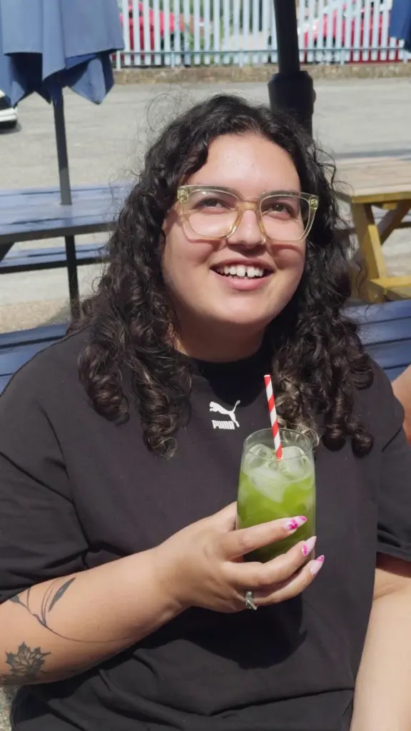 Smiling person holding a glass of iced green tea outdoors