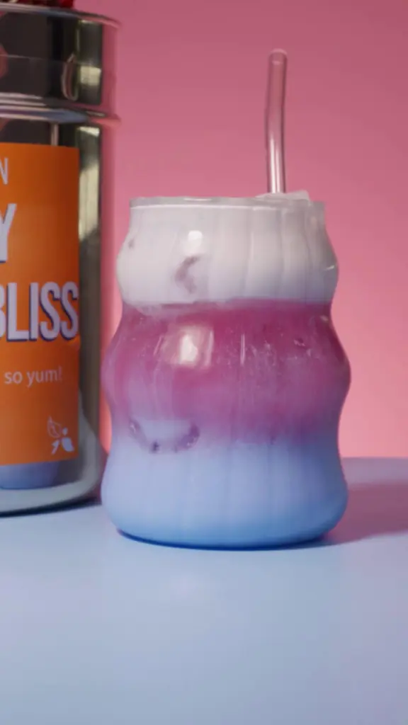 Purple and pale blue layered iced drink topped with white foam in a curved glass