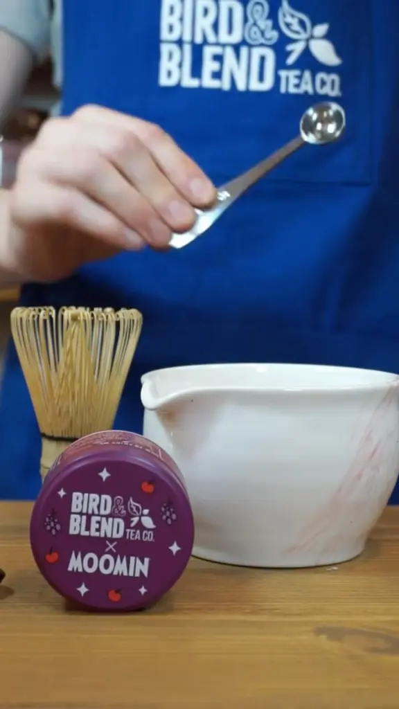 Purple Moomin tin beside a bamboo whisk, ceramic bowl, and measuring spoon