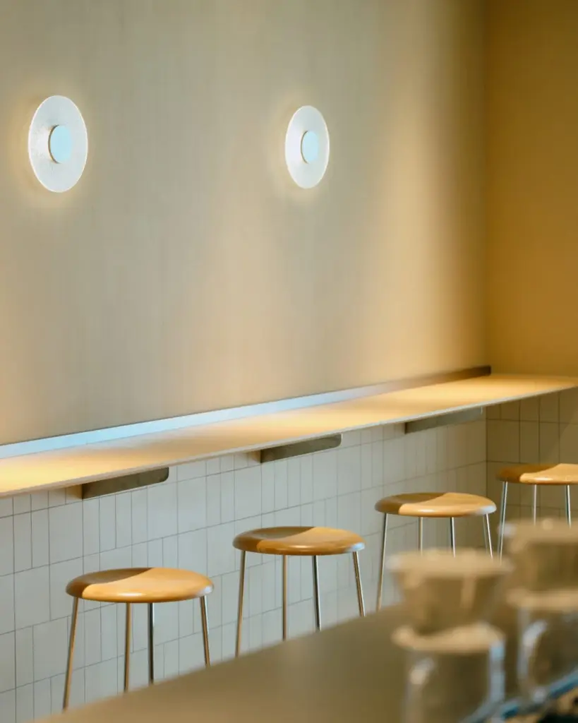 Wooden stools beneath a slim counter and two circular wall lights