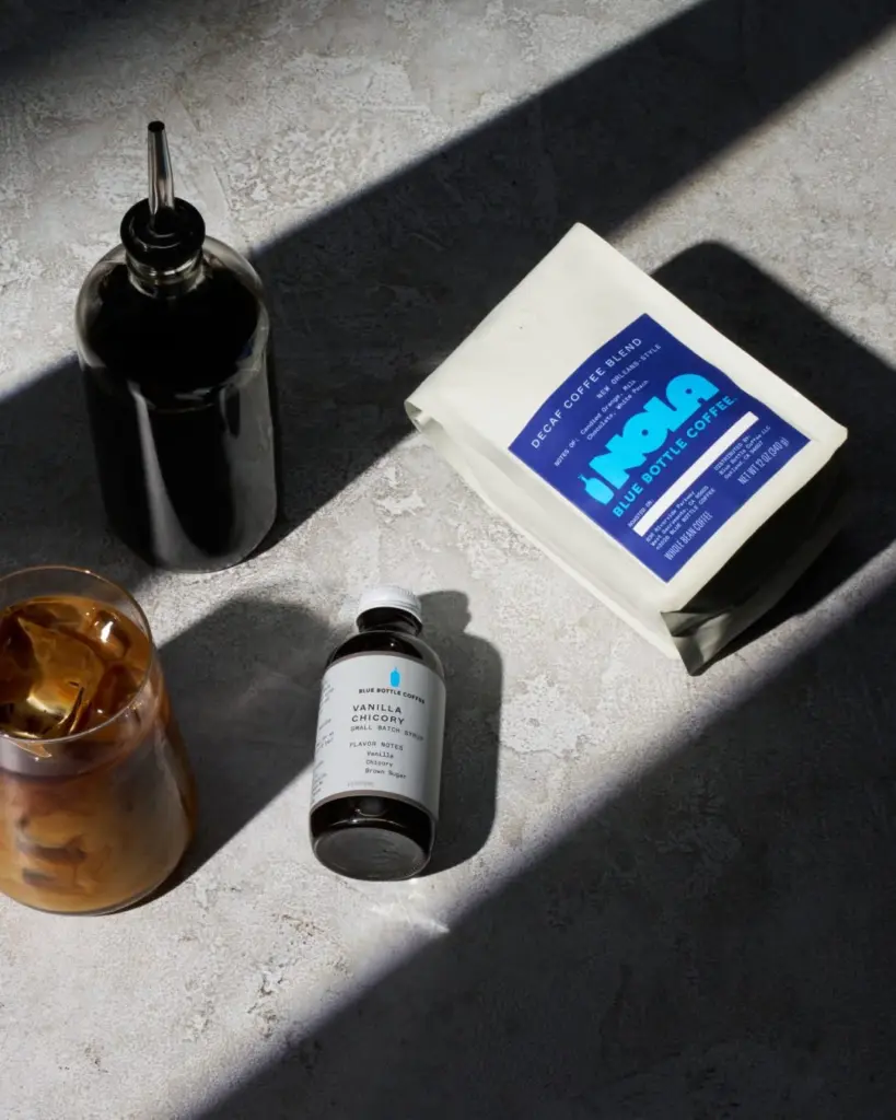 Iced milky coffee beside decaf coffee, vanilla chicory syrup, and a dark bottle