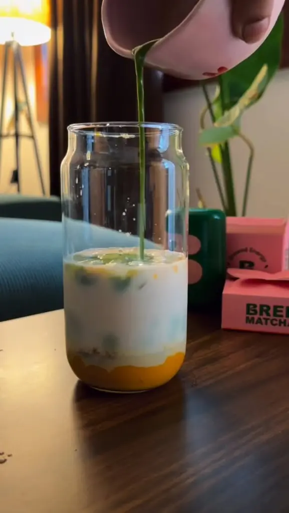 Green matcha poured from a pink pitcher into a layered iced drink