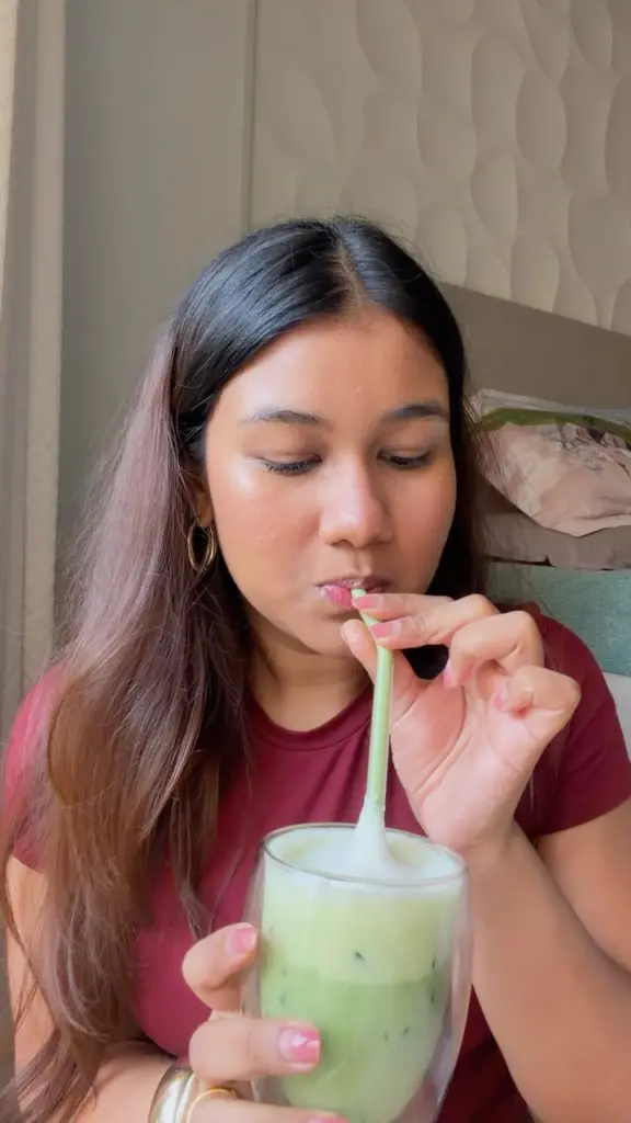 Woman sipping a pale green iced drink through a green straw