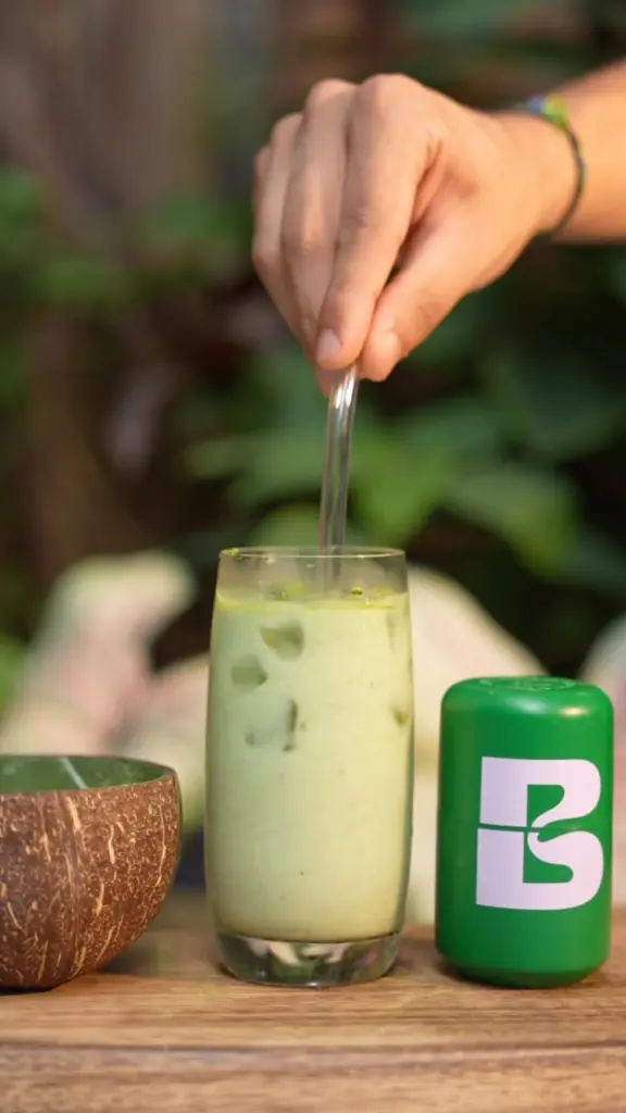 Hand stirring a pale green iced drink beside a green Bree container