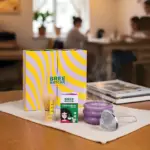 Bree Matcha gift kit with striped purple and yellow box, bamboo whisk, ceremonial matcha carton, purple bowl and mesh strainer on a woven mat