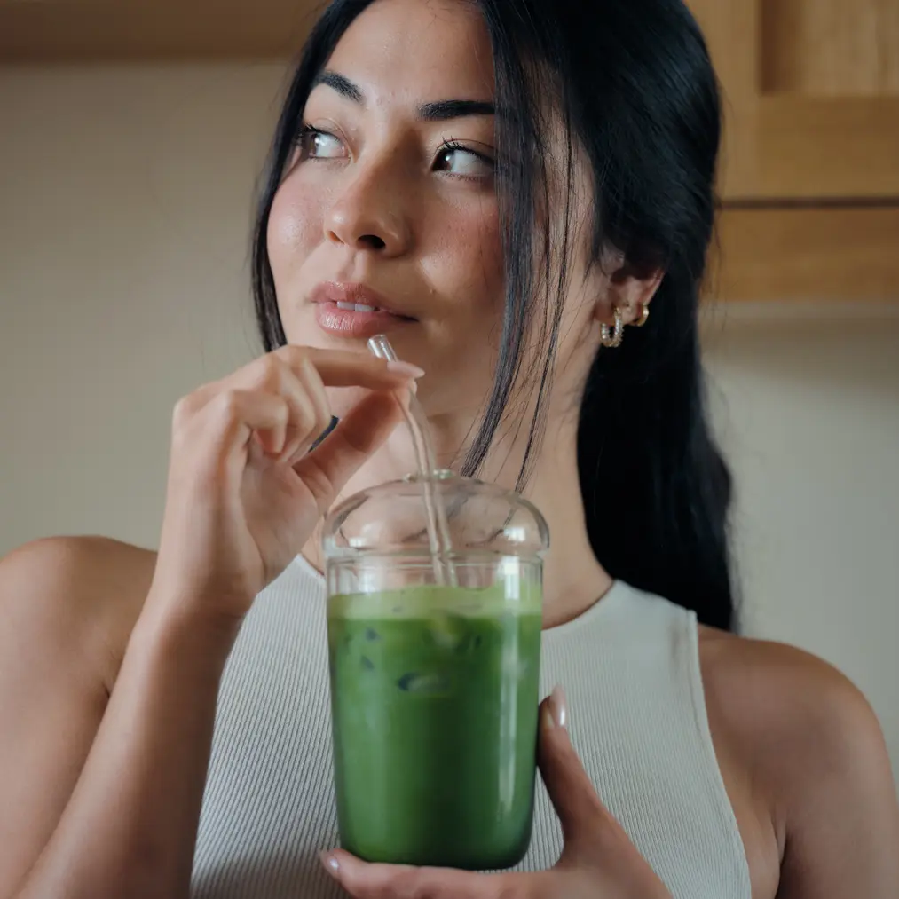 Woman holding a clear cup of iced green matcha with a glass straw