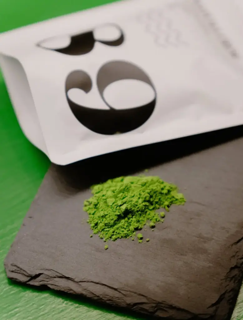 Green matcha powder on a dark stone slab beside a white No. 89 pouch