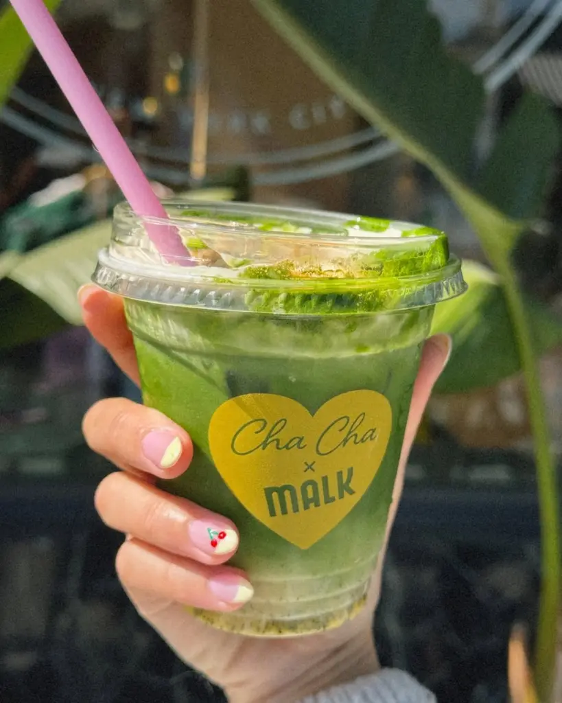 Hand holding a green iced drink with a pink straw