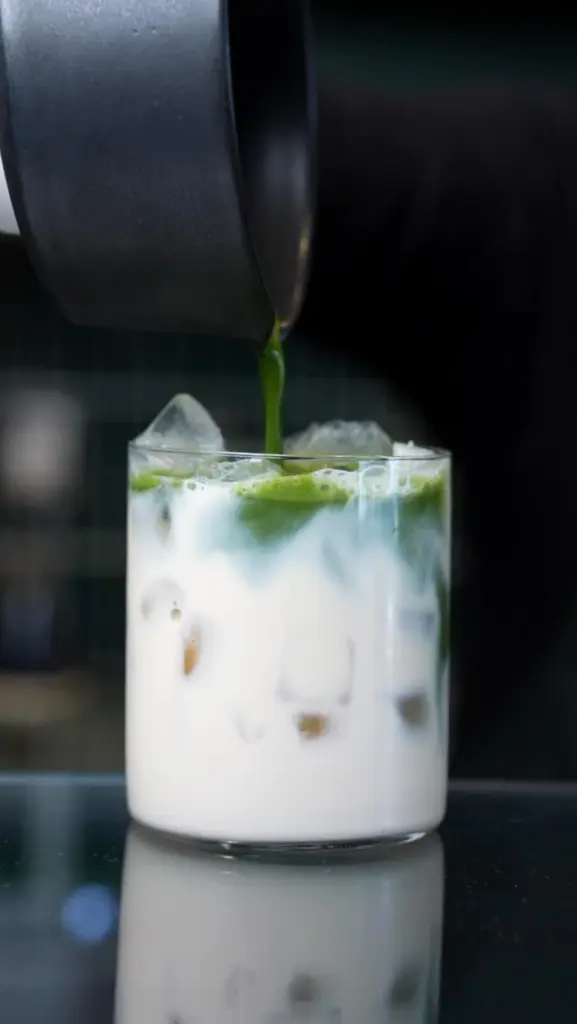 Green matcha pouring into a glass of white iced drink