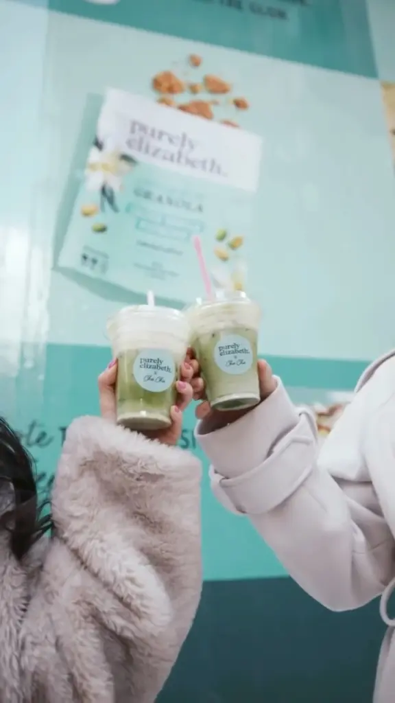 Two hands holding green drinks together in clear cups