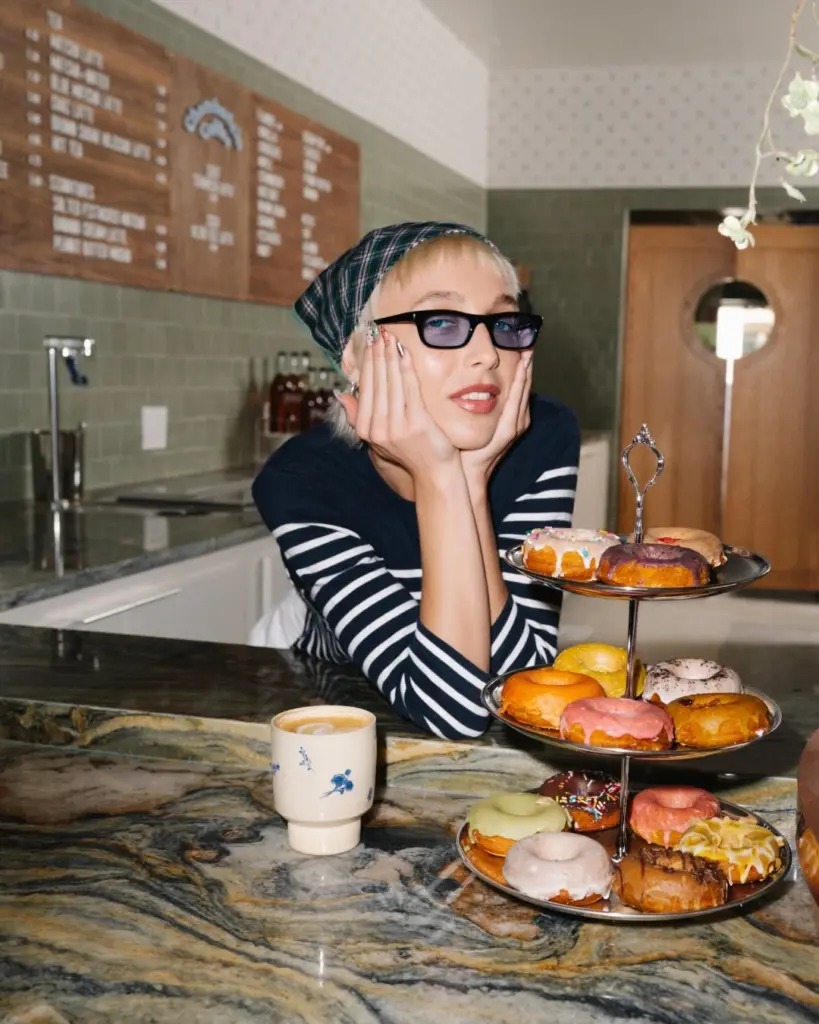 Person leaning beside a tiered tray of colorful donuts and a ceramic coffee cup