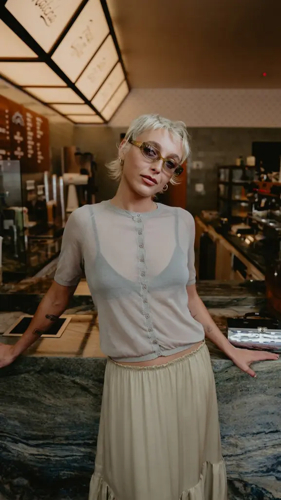 Person with short blond hair and tinted glasses leaning against a marble café counter