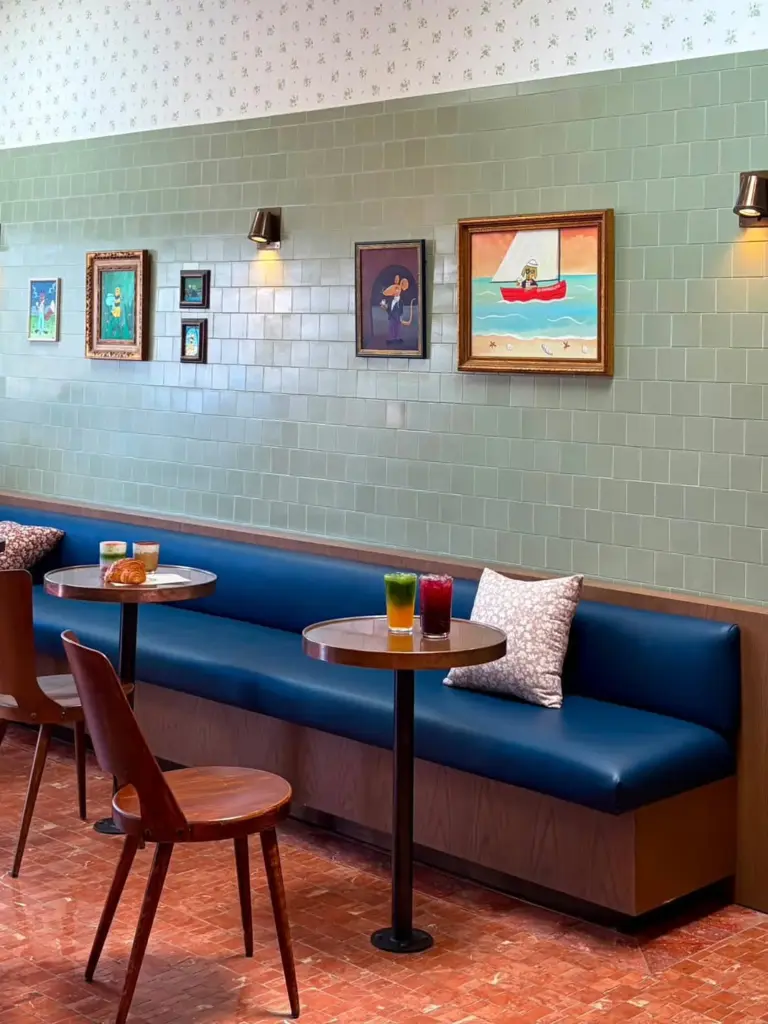 Blue café banquette with colorful drinks on round tables beneath framed artwork