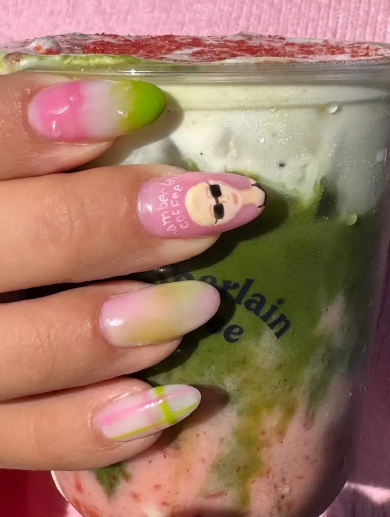 Manicured hand holding a chilled layered green, white, and pink drink
