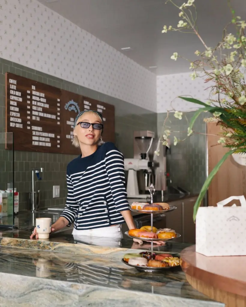 Person holding a ceramic cup beside a three-tier tray of colorful donuts
